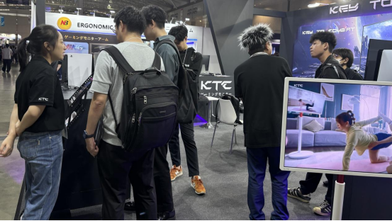 People gathered at the KTC exhibition booth, with one monitor displaying a woman doing a home workout.